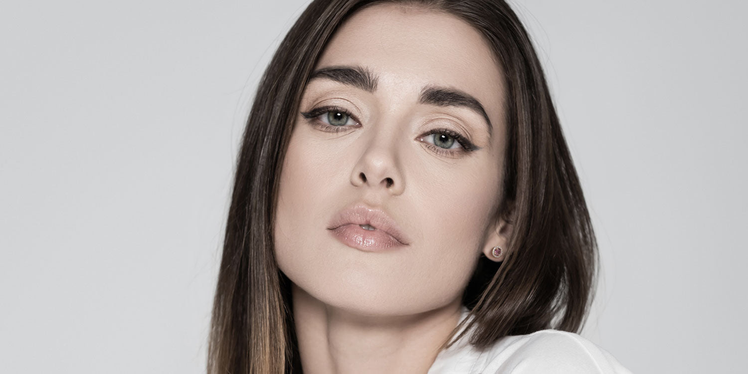 Junge Frau mit braunen Haaren und grünen Augen in weißem Top trägt kleine runde Ohrstecker 