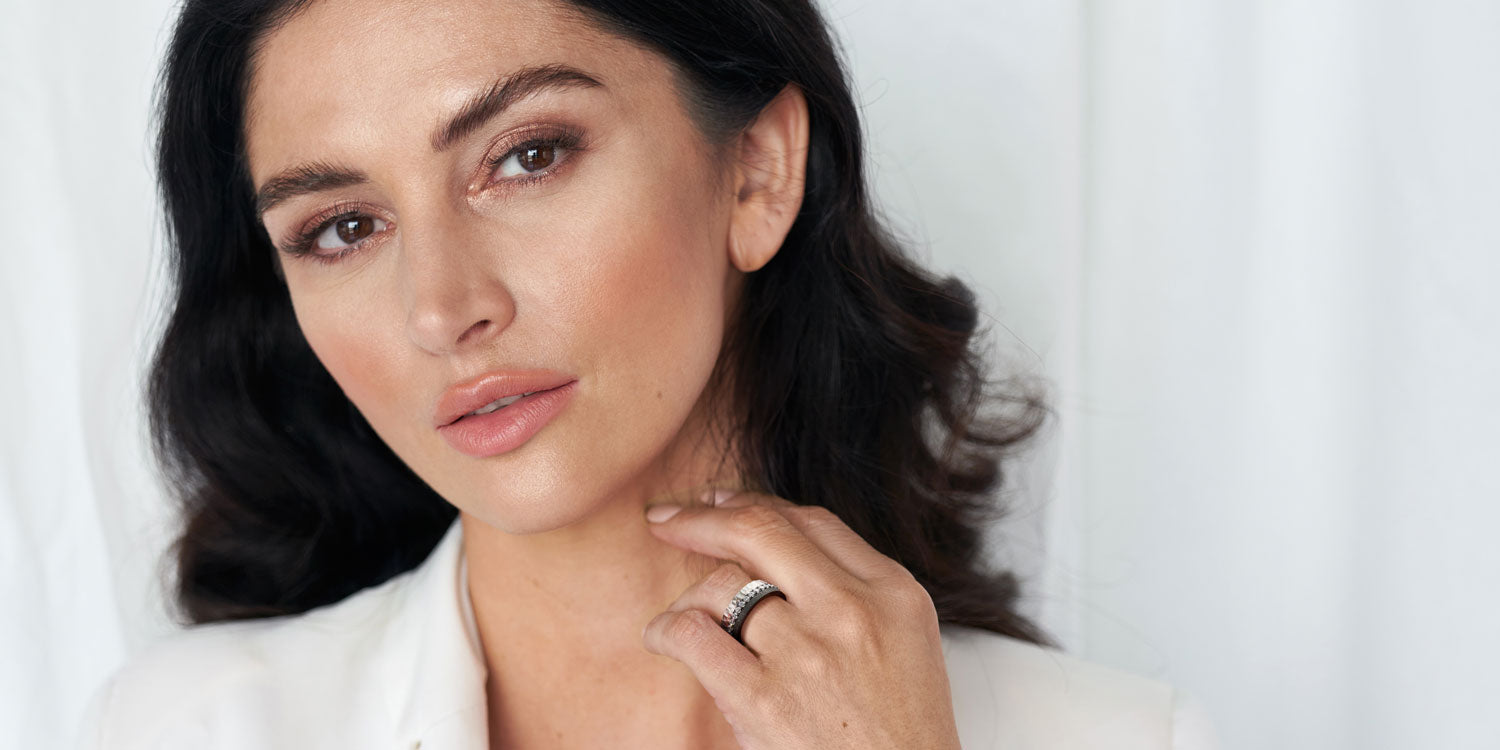 Elegante Frau mit dunklen Haaren in weißem Outfit trägt mehrere Ringe am Ringfinger