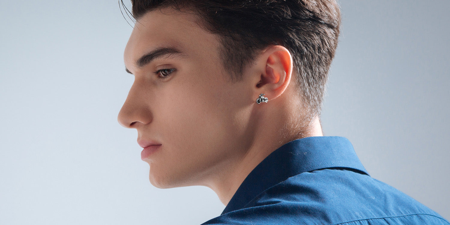 Junger Mann im Profil trägt silberne Motorrad-Ohrstecker in blauem Hemd vor grauem Hintergrund