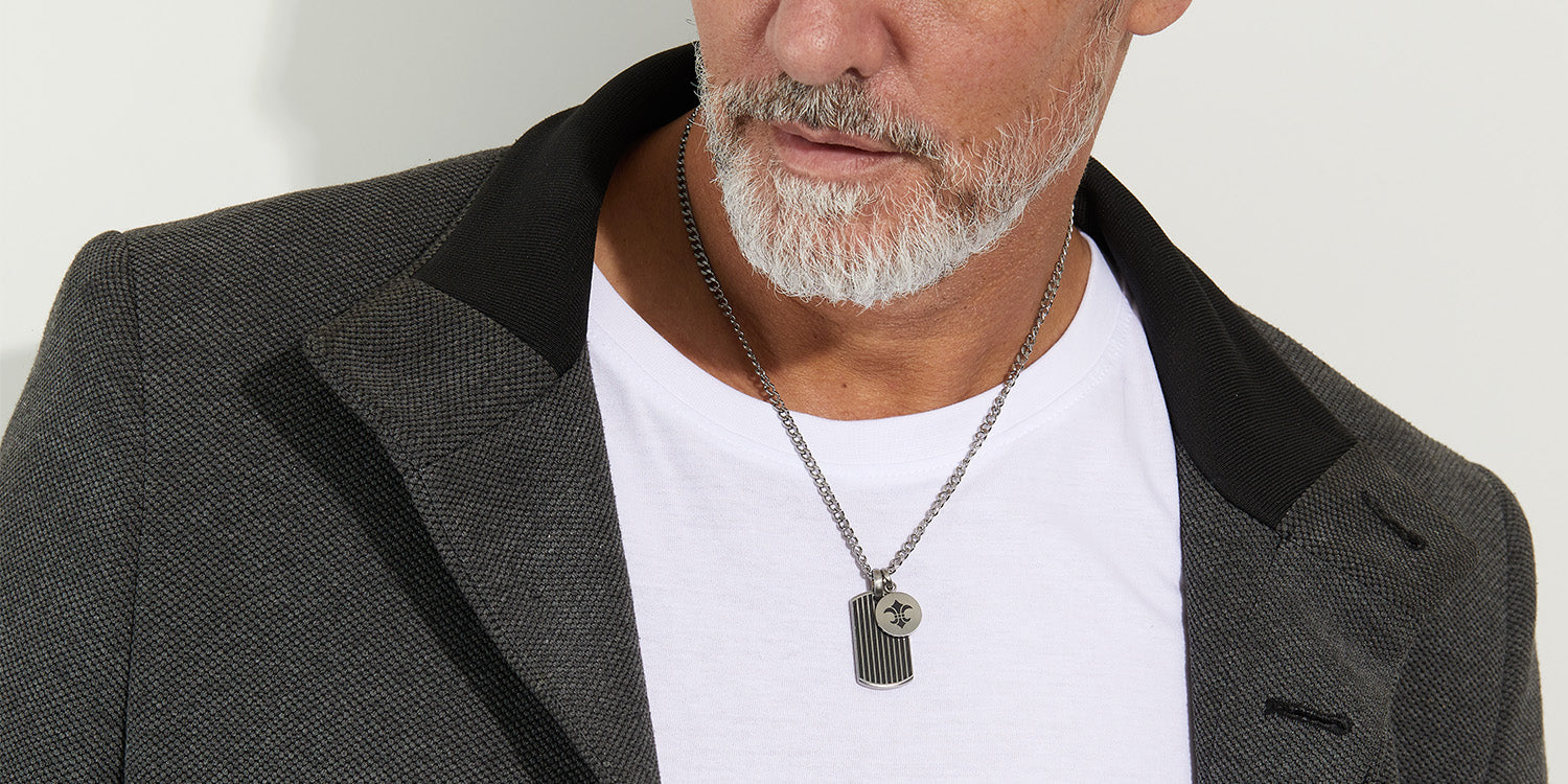 Mann trägt eine silberne Halskette mit zwei markanten Anhängern, kombiniert mit weißem T-Shirt und dunklem Blazer